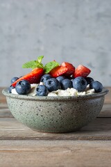A bowl with cottage cheese, yogurt, fresh berries (blueberries, strawberries) and fresh mint on a wooden background. Delicious breakfast, healthy food.