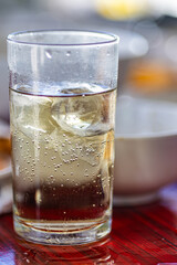 A glass of ice water sits on a table. The glass is half full and the ice cubes are floating in the water