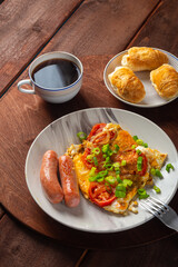 Eggs with tomatoes and sausages in a plate on a wooden table of coffee and croissants on a round stand