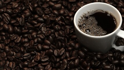 Top view of coffee or espresso with piles of coffee beans. Close up of fresh roasted coffee bean scatter around wooden table with cup of americano and aromatic stream and smoke from seed. Comestible.