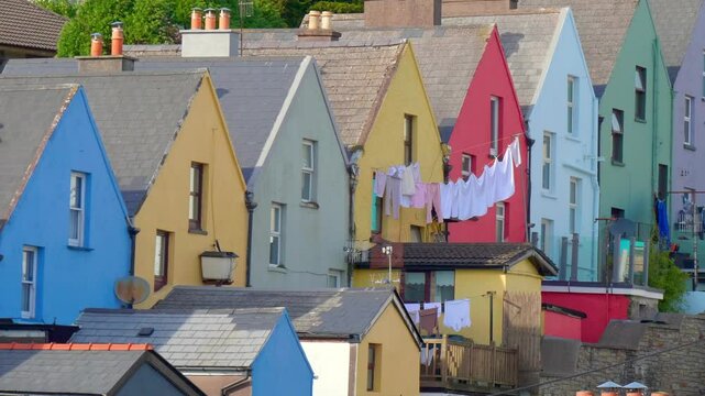 A row of houses with colorful walls, black window frames, and slate roofs. A clothesline stretches across the back of the houses, with white and pink clothes hanging on it.