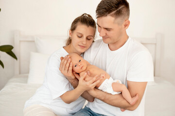 young parents with a newborn baby hug and kiss, happy mom and dad admiring the baby at home on the bed, a happy family caring for a small child, a place for text