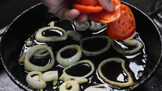 A woman's hand places trmaty circles into a frying pan with fried onions. Medium shot.