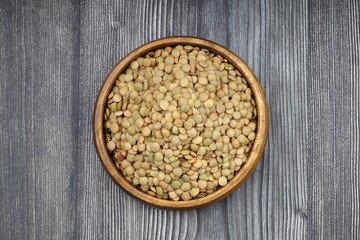 Green lentils in wooden bowl on wooden table background. Top view, copy space. Flat lay.