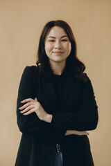 Fototapeta premium Pretty Asian young woman in turtleneck and jacket posing on beige background, looking at camera.