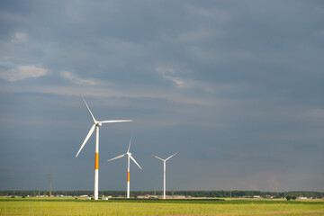 Distant white wind turbines against a dramatic cloudy sky. Meadow in the foreground, taken late afternoon