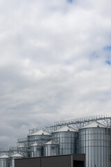 Obraz premium Steel grain silo against a dramatic, cloudy sky. Modern agriculture buildings photographed in the day .