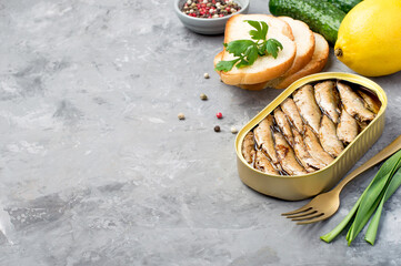 Tin can with sprats, bread, vegetables and herbs on a dark background, close-up. Horizontal, space...