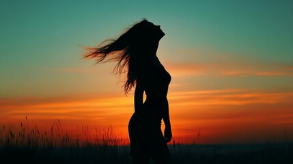 Silhouette of a woman standing in a field at sunset with her hair blowing in the wind.