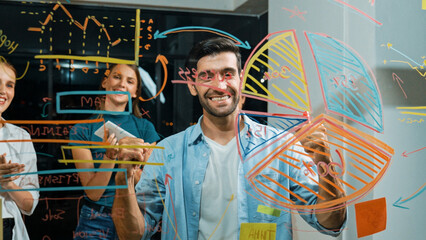 Happy smart businessman celebrate successful project at glass wall while explain marketing strategy to business people. Professional male leader show financial statistic at glass wall. Tracery