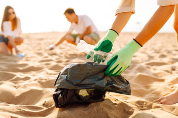 Group of young adults cleaning up plastic waste on a sunny beach during the day, promoting...