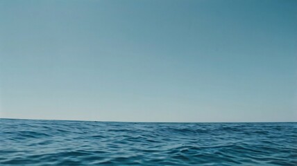 Fototapeta premium The view offers a peaceful seascape with gentle waves reflecting the light blue sky. The vast horizon stretches endlessly, creating a serene and calm atmosphere