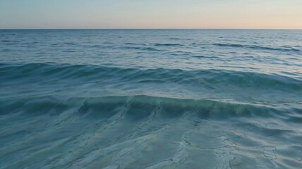 Obraz premium Soft waves rhythmically lap against the shoreline, reflecting a tranquil gradient sky as the sun sets, creating a peaceful coastal atmosphere