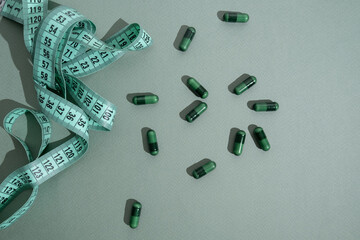 Measuring tape and tablets, vitamins on a colored background with space for text. Concept of losing weight, dieting, burning fat, healthy eating. 
