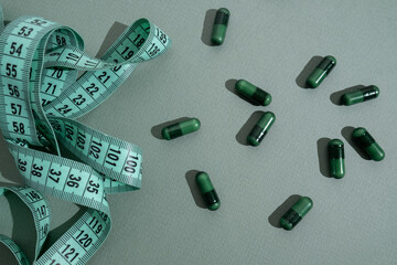 Measuring tape and tablets, vitamins on a colored background with space for text. Concept of losing weight, dieting, burning fat, healthy eating. 