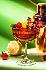 Tomato juice and vodka alcoholic cocktail drink with smoked bacon, celery, hot sauce, pickles and ice in glass with salt and red pepper. Green background, hard light