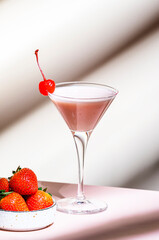 Delicious summer cocktail with vodka, liqueur, cream, strawberries and ice  with cocktail cherry. Beige background, hard light