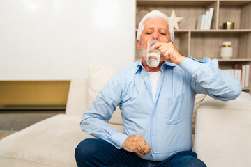 Senior man holding glass drinking fresh water at home. Mature old senior thirsty grandfather takes...