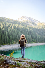 Enjoying a peaceful moment, a woman sits on a rocky ledge while gazing at the stunning turquoise lake surrounded by lush mountains during daylight. Active lifestyle.
