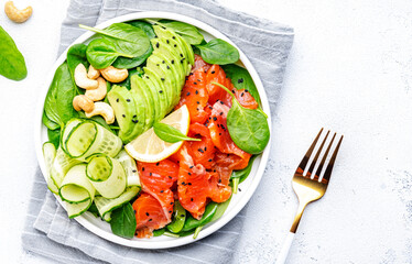 Keto salad with salmon, avocado, spinach, cucumber, sesame seeds  and cashew nuts.. White background, top view