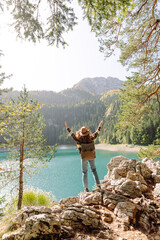 Enjoying a peaceful moment, a woman sits on a rocky ledge while gazing at the stunning turquoise lake surrounded by lush mountains during daylight. Active lifestyle.