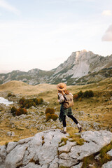 Obraz premium A young woman with a wide-brimmed hat enjoys a sunny afternoon in the mountains while sitting on rocks with a picturesque landscape behind her. Eco tourism. Active lifestyle.