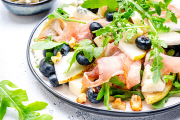 Delicious salad with pears, blueberries, blue cheese, smoked ham, arugula and walnuts. White background, top view