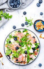 Delicious salad with pears, blueberries, blue cheese, smoked ham, arugula and walnuts. White background, top view