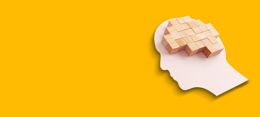 Mental health concept. Human brain made of wooden cubes on yellow background.