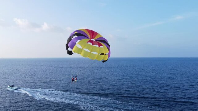 Drone view of fun water sport activity as couple parasails behind boat on ocean