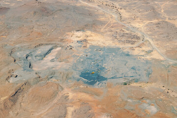 An open pit mine or quarry with machinery, excavators, bulldozers, and trucks digging and extracting black rock coal, charcoal or smut in the middle of the Sahara desert arid land reg. 
