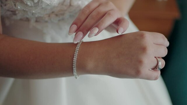 Bride adjusting a delicate diamond bracelet on her wrist, wearing a white wedding dress