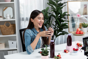 Smiling young beautiful Asian reviewing tasty mixed strawberry and cherry juice detox drinks,...