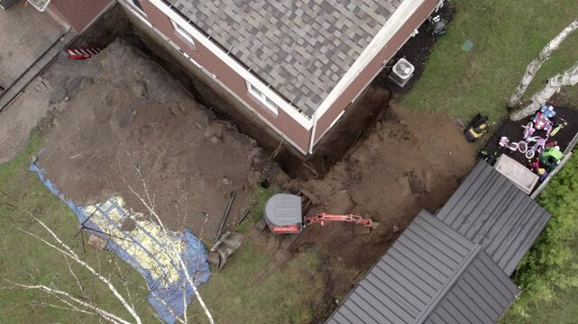 Contractor digs up foundation with mini excavtor for repairs - aerial view