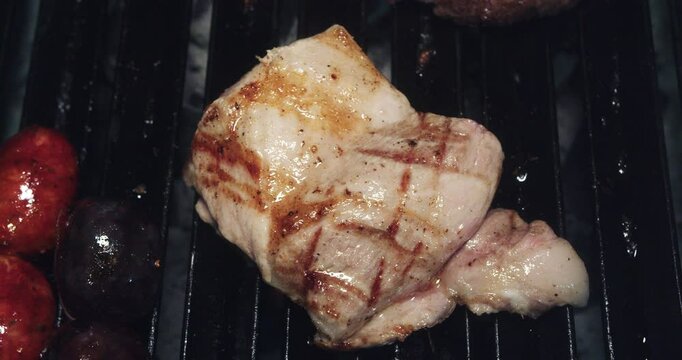 Beautiful slow motion shot of a piece of pork roasting on a grill next to beef and sausage inside a restaurant kitchen.
