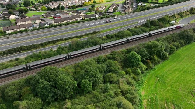 Railway, Newry, County Armagh, Northern Ireland, September 2022. Drone tilt's up as the Belfast to Dublin Enterprise train heads south over Carnagat Lane with A1 road and Newry town in the background.