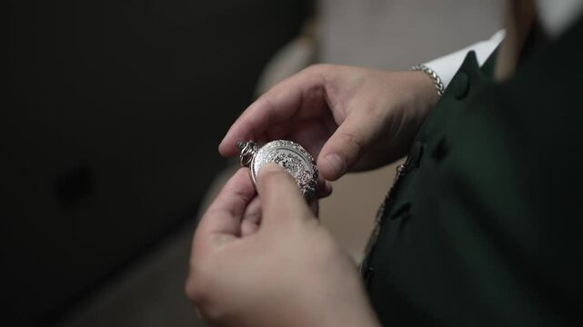 Hands holding a silver pocket watch, carefully examining the intricate details