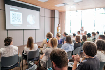 Audience attending business presentation in modern conference room. Participants focused on speaker and screen in professional setting.