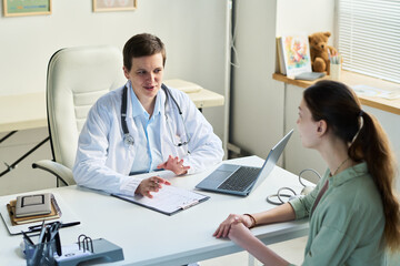 Doctor consulting patient in modern medical office, discussing health concerns and treatment options. Medical equipment, notebook and stethoscope on desk