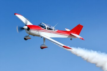 A low-flying red and white plane trails smoke against a clear blue sky.