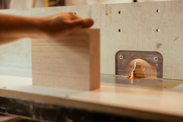 Man putting lumber block through spindle moulder, creating smooth and precise edges on wooden pieces. Joiner using heavy machinery to craft strong and seamless joints for furniture and structures
