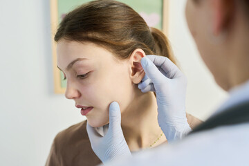 Medical professional wearing gloves examining patient's ear during ear check-up in clinic focusing on detail. Close-up shot of medical procedure in sterile environment