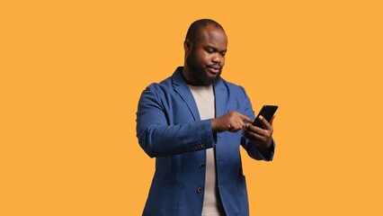 Portrait of energetic happy man holding smartphone celebrating, throwing fists in air from excitement. Overjoyed BIPOC person reading good news on phone, cheering, studio background, camera B