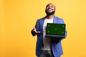 Portrait of relaxed carefree man pointing towards green screen laptop, doing endorsement. Delighted tech reviewer giving positive feedback to chroma key notebook, isolated over studio background