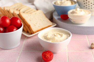 Bowl of tasty cream cheese on pink tile background