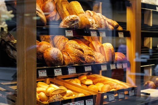 German bakery counter showcase display with many different baked bread price tags and names.  Fresh hot crusty pastry product assortment variety at european retail grocery store market