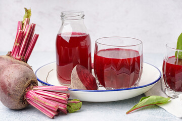 Glass and bottle of fresh beetroot juice on light background