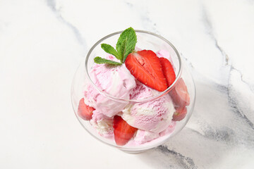 Glass bowl of strawberry ice cream with mint on grunge background