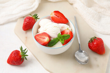 Bowl of vanilla ice cream with strawberries, mint and spoon on white table