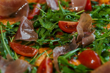 Pepperoni pizza with arugula and prosciutto. Meat pizza with cheese, cherry tomatoes and fresh arugula on a white background